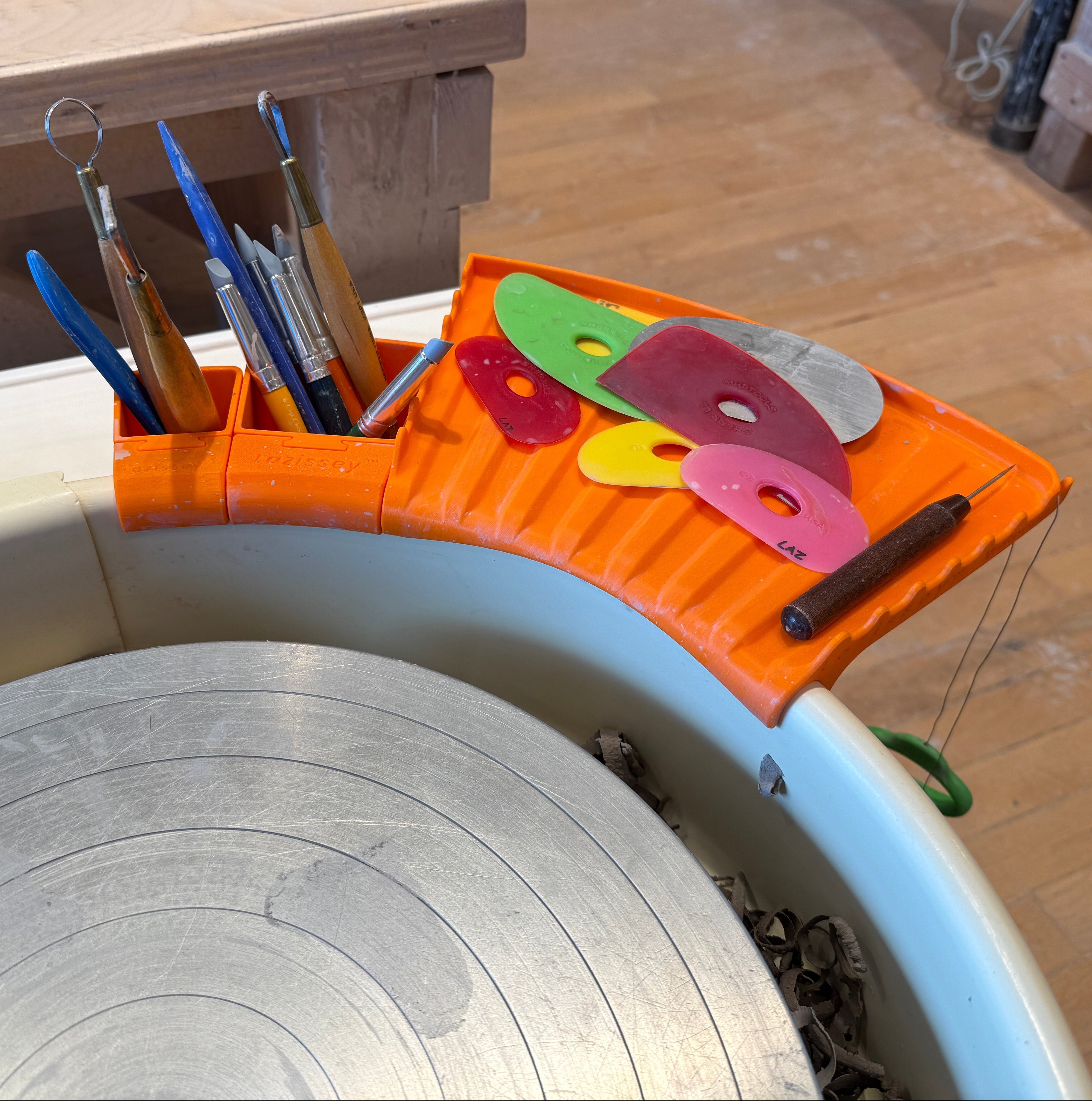 Orange tool holder with various tools on a potter's wheel in a pottery studio.